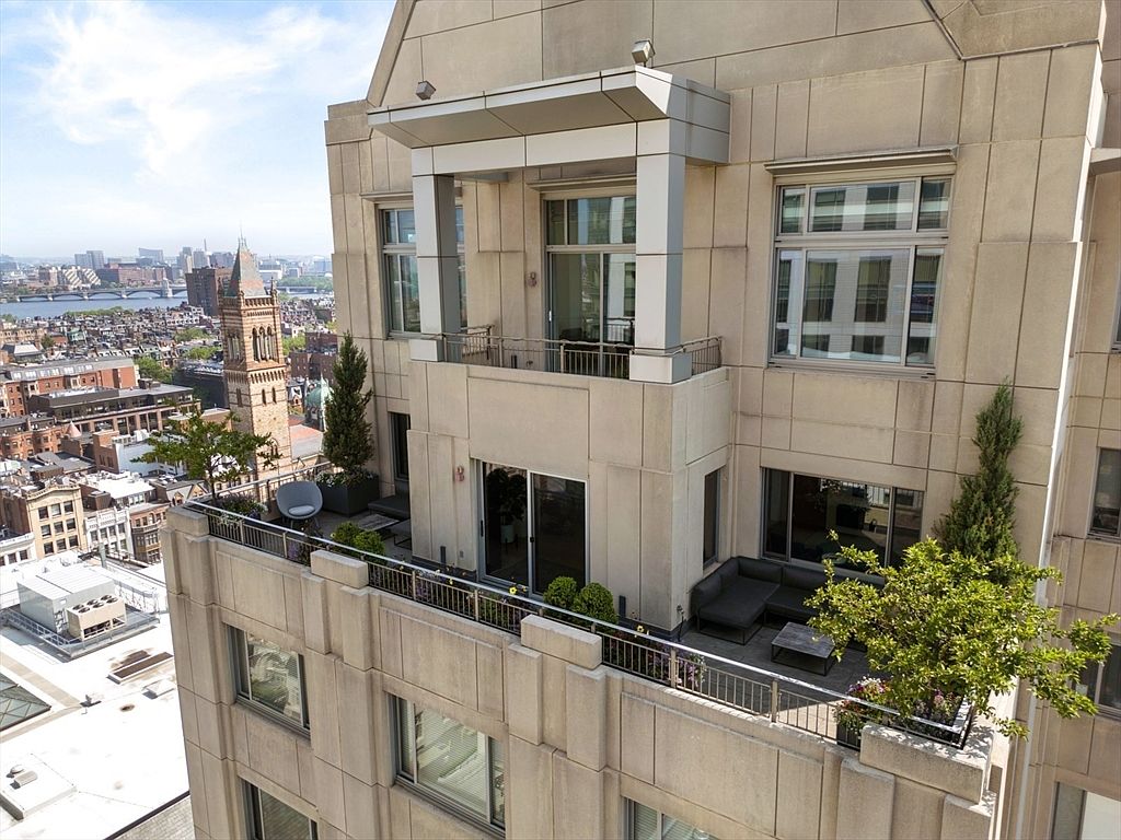This image showcases a luxurious penthouse balcony with stunning city views. The balcony features stylish outdoor furniture, lush greenery, and a sleek railing. The building's architecture is modern and sophisticated, emphasizing the high-end nature of the property.