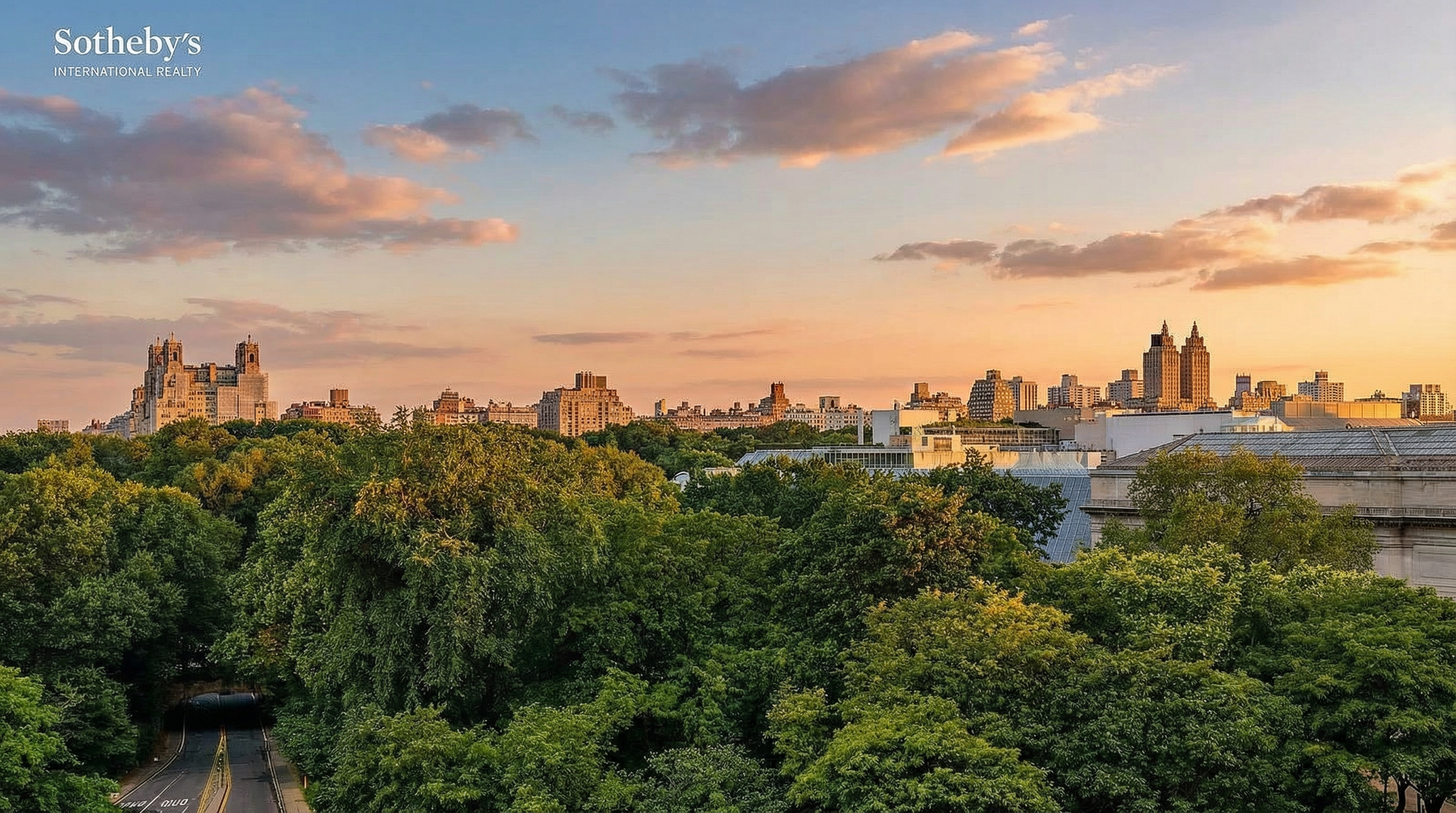 This elevated, wide-angle shot captures a lush, expansive park landscape in the foreground, transitioning into a dense urban skyline under a bright, clear blue sky with scattered clouds. A winding road curves through the trees on the left, while the architectural details of city buildings are visible in the distance, suggesting a prime location near a major metropolitan green space. The perspective provides a serene and prestigious view, emphasizing the property's proximity to nature and city life.