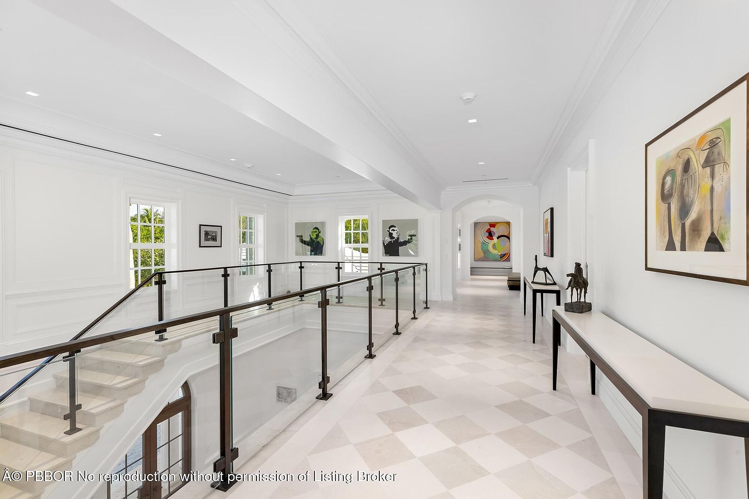 This interior shot showcases a bright and spacious hallway with a staircase. The hallway features a checkered tile floor, white walls adorned with modern art, and a glass-paneled railing along the staircase. The space is well-lit, creating an airy and elegant atmosphere, perfect for highlighting the home's architectural details and sophisticated design.