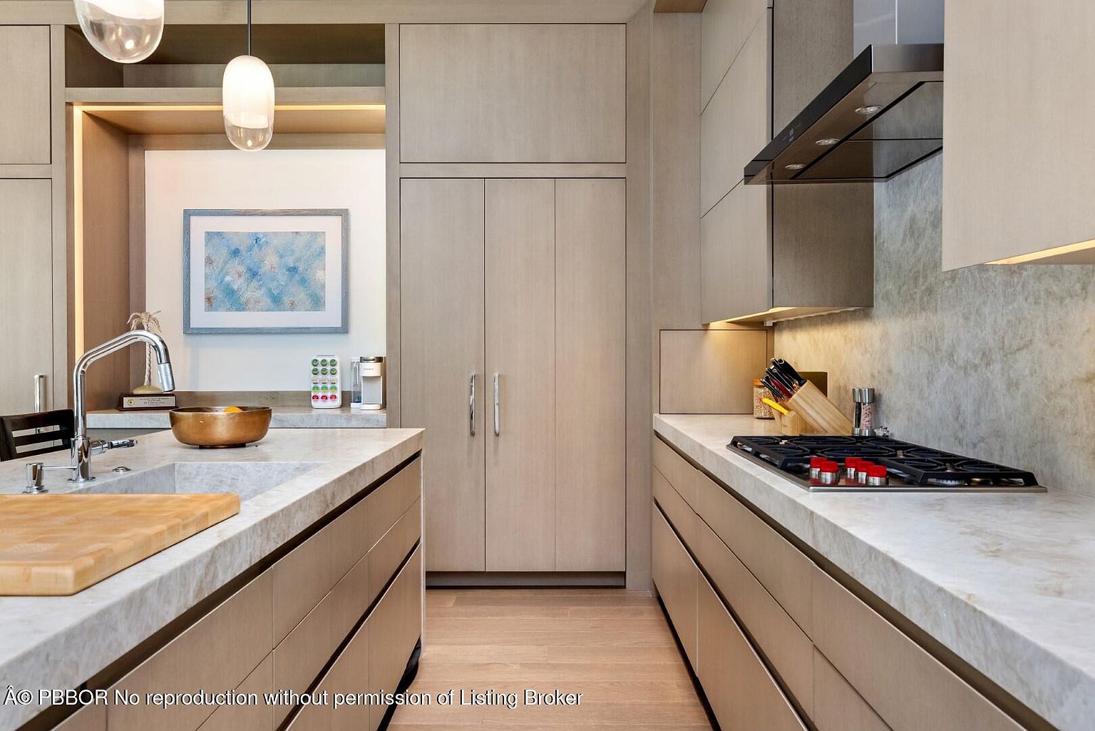This is a well-lit, modern kitchen featuring light wood cabinetry and marble countertops. The kitchen is designed with a clean, minimalist aesthetic, showcasing a gas cooktop, stainless steel range hood, and a deep sink with a modern faucet. The overall impression is one of understated elegance and functionality.