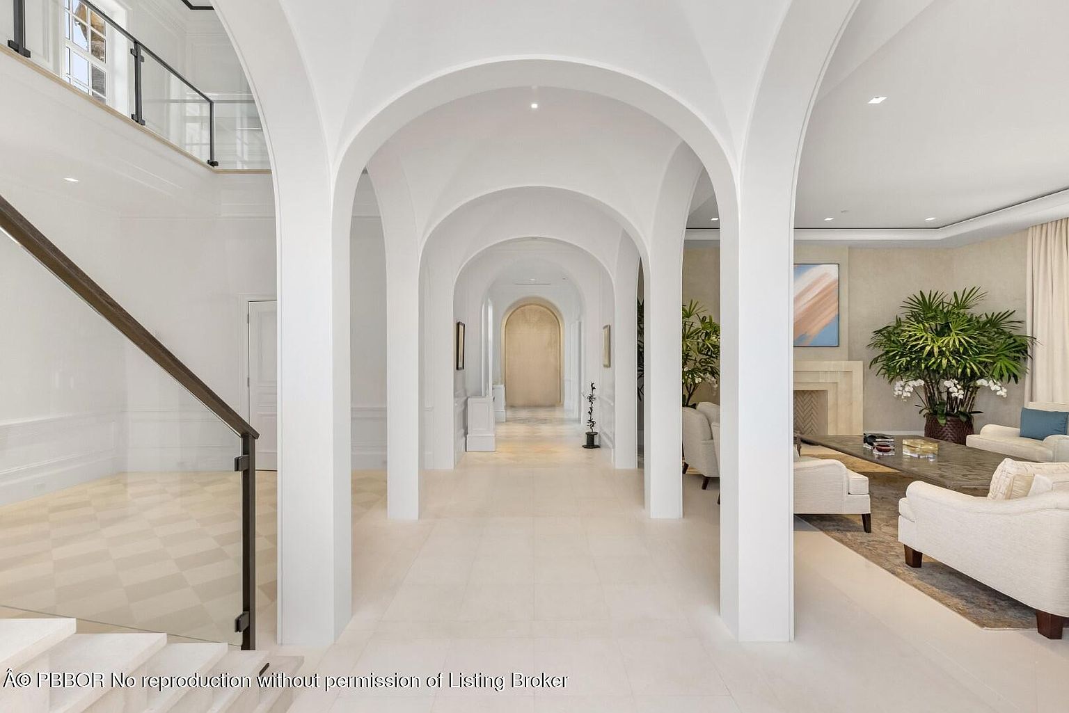 This interior shot showcases a grand hallway with a series of elegant, arched openings leading into other rooms. The hallway features pristine white walls and light-colored flooring, creating a bright and airy atmosphere. A staircase with a glass railing is visible on the left, adding a modern touch to the classic architectural design.