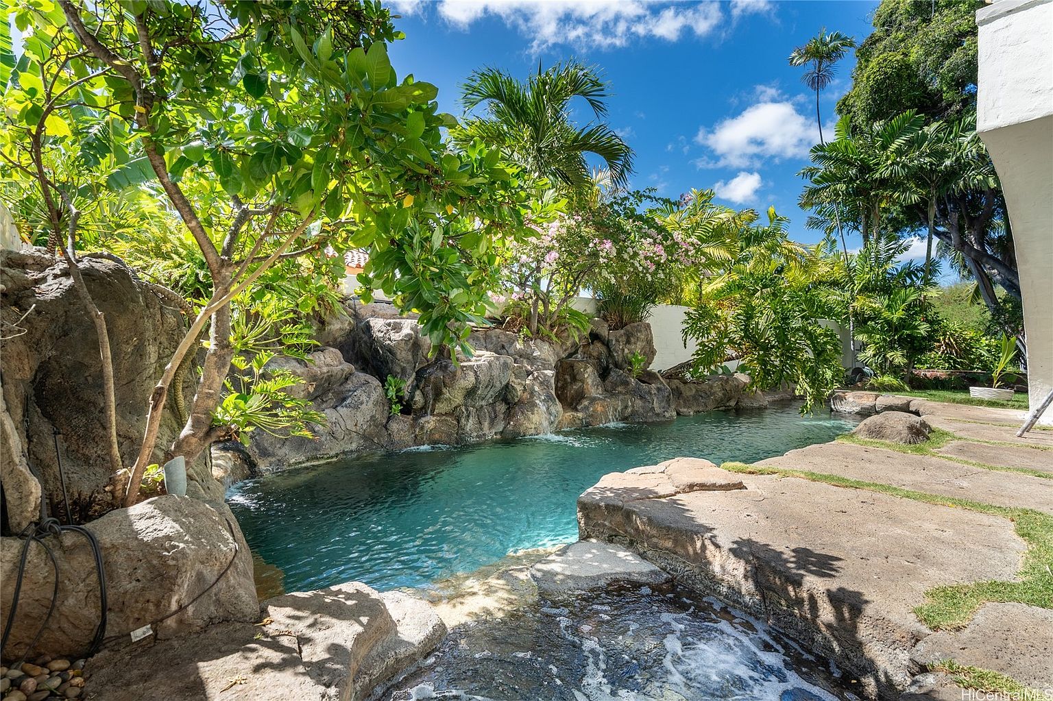 This image showcases a luxurious pool and spa area, surrounded by lush tropical landscaping and rock formations. The clear blue water invites relaxation, while the natural stone accents create a serene and private oasis. The scene evokes a sense of tranquility and upscale outdoor living.