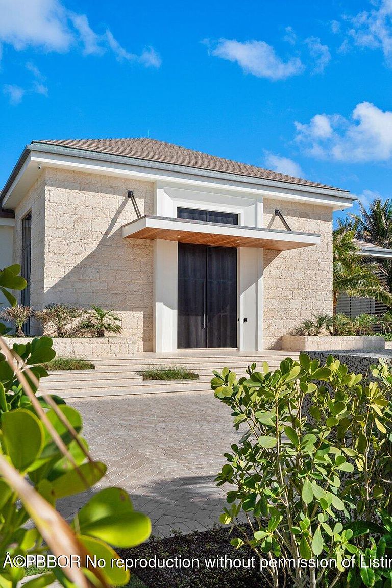 This image showcases the grand entryway of a modern home, featuring a striking stone facade and a dark, double-door entrance. A cantilevered wooden awning provides shelter, while manicured landscaping adds to the curb appeal. The overall impression is one of sophisticated elegance and architectural detail.