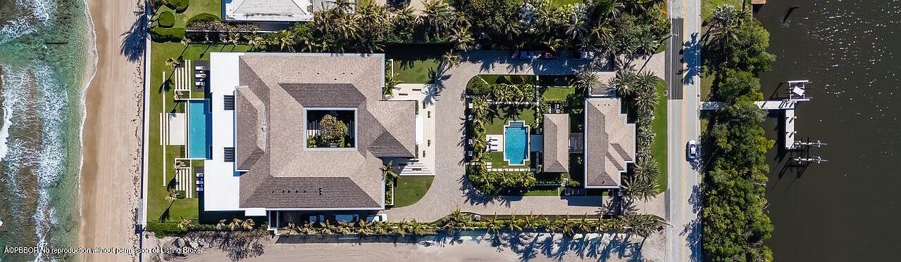 This aerial shot showcases two luxurious beachfront properties with meticulously landscaped grounds, including pools and manicured lawns. The architectural style is modern and elegant, with clean lines and neutral color palettes. The properties offer direct access to the beach on one side and a waterway with a private dock on the other, emphasizing exclusivity and waterfront living.