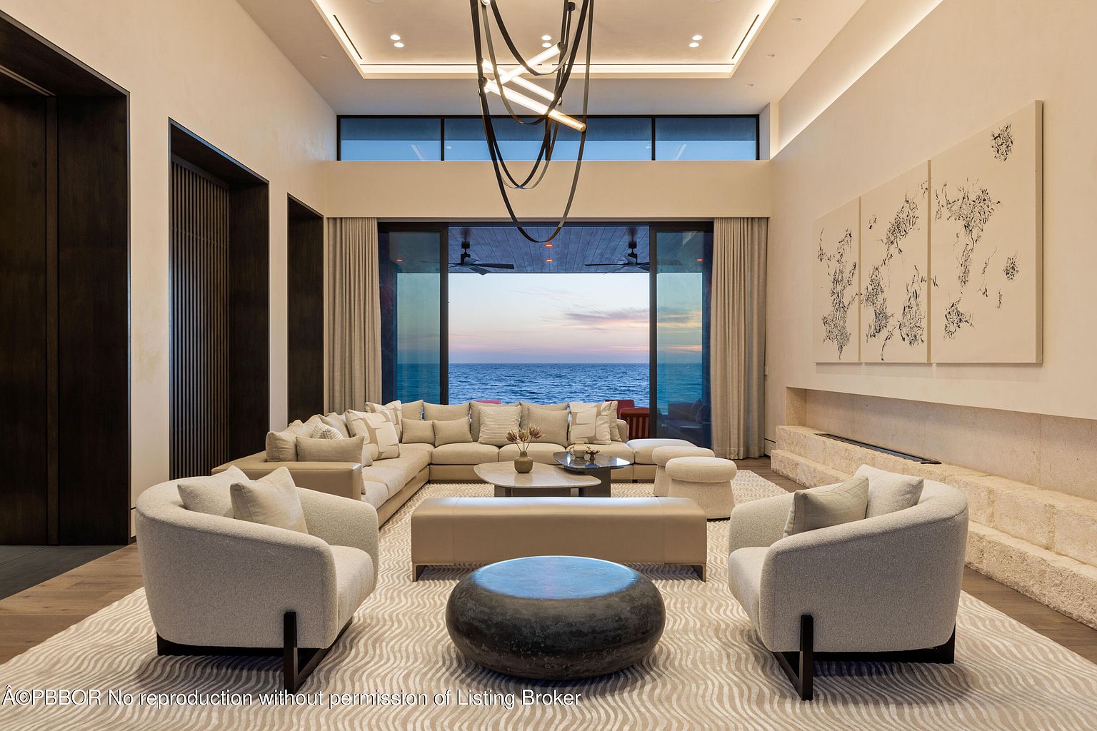 This is a luxurious living room with a large sectional sofa, two armchairs, and a unique coffee table. The room features a modern fireplace, artwork, and floor-to-ceiling windows offering an ocean view. The overall design is contemporary and elegant, creating a comfortable and sophisticated space.