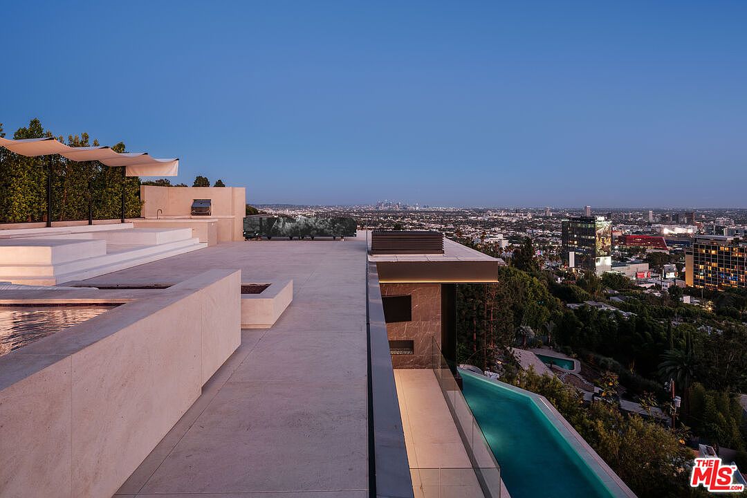 This stunning, modern rooftop terrace offers an expansive, unobstructed panoramic view of the city skyline at dusk. The space features a sleek infinity-edge pool, minimalist concrete decking, and integrated lounge areas with contemporary shade structures. The cinematic perspective captures the seamless transition between the luxurious outdoor living space and the vibrant urban landscape below.