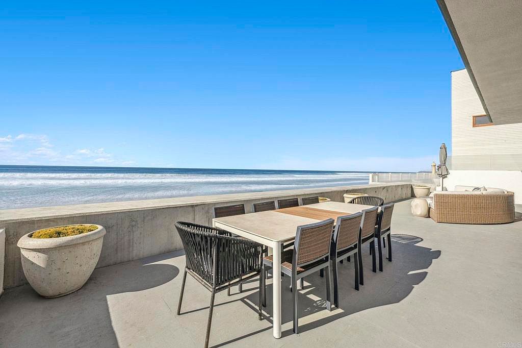 This image showcases a luxurious outdoor patio or deck area with ocean views. A large dining table with modern chairs is centrally located, suggesting an ideal space for entertaining. The patio also features a comfortable lounge area and decorative planters, enhancing the overall ambiance of relaxation and sophistication.