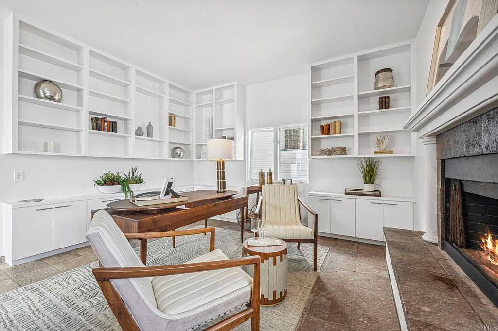 This interior shot showcases a well-appointed office or study, featuring custom built-in shelving and cabinetry in a crisp white finish. A wooden desk serves as the focal point, complemented by stylish chairs and a patterned area rug. The room exudes a sophisticated and functional ambiance, ideal for a home office setting.