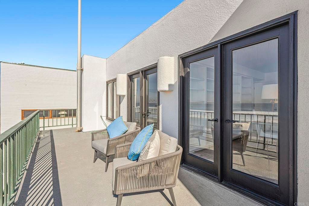 This image showcases a charming balcony featuring two stylish chairs with blue pillows, creating an inviting outdoor seating area. The balcony is adjacent to a building with large glass doors, allowing for ample natural light and views. The overall impression is one of relaxation and modern comfort, perfect for enjoying the outdoors.