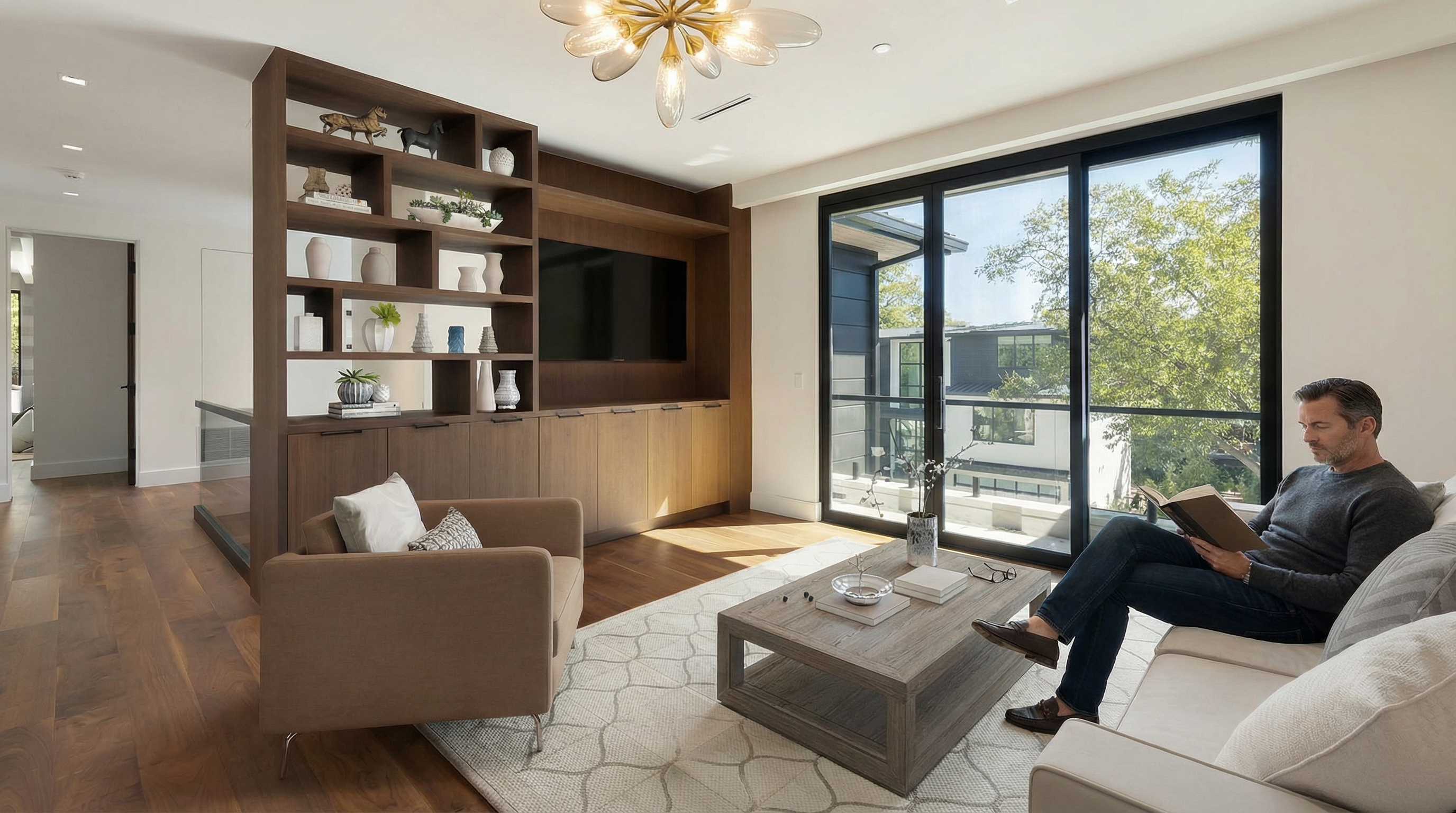 This modern, elegantly furnished living room features a striking custom wood room divider with integrated shelving and a built-in television console. The space is highlighted by a sophisticated gold petal pendant light, a contemporary gray coffee table, and large sliding glass doors that provide abundant natural light and a view of the outdoors. A comfortable seating area with an armchair and sofa, along with warm hardwood flooring, creates a welcoming and refined atmosphere.