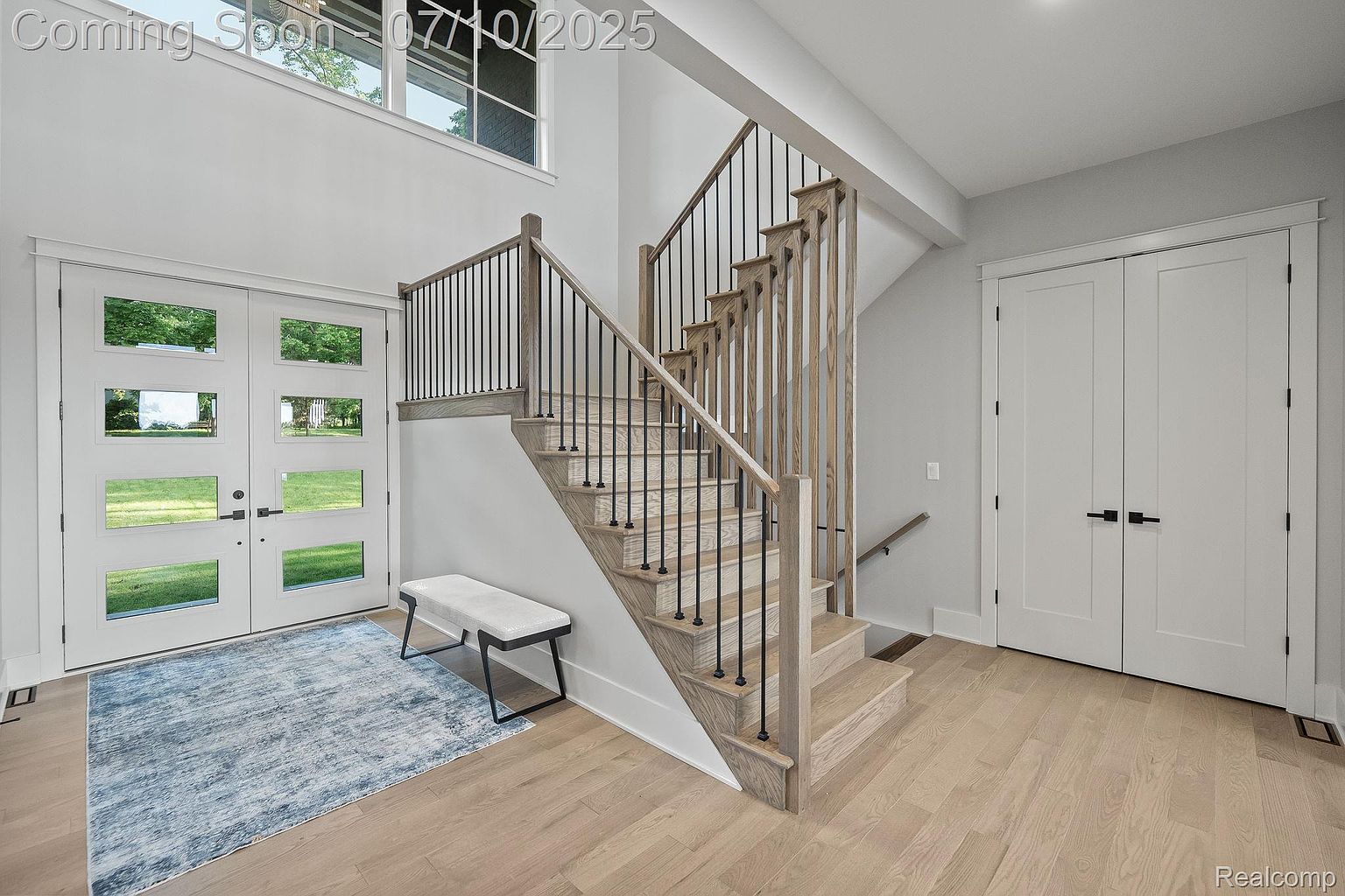 This interior shot showcases a modern hallway with a staircase as a focal point. The staircase features light wood steps and black metal railings, complemented by a light-colored wood floor. A white bench sits near the entryway, adding a touch of elegance and functionality to the space.