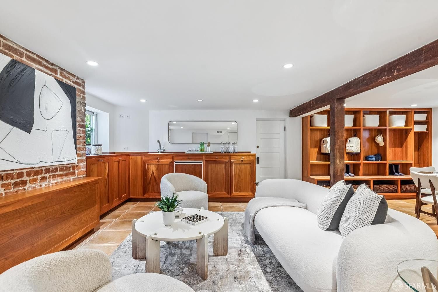 This interior shot showcases a stylish living room with a blend of modern and rustic elements. The room features a white curved sofa, a round coffee table, and comfortable armchairs, all set on a patterned rug. Wooden cabinetry and a brick accent wall add warmth and character to the space, creating an inviting and sophisticated atmosphere.