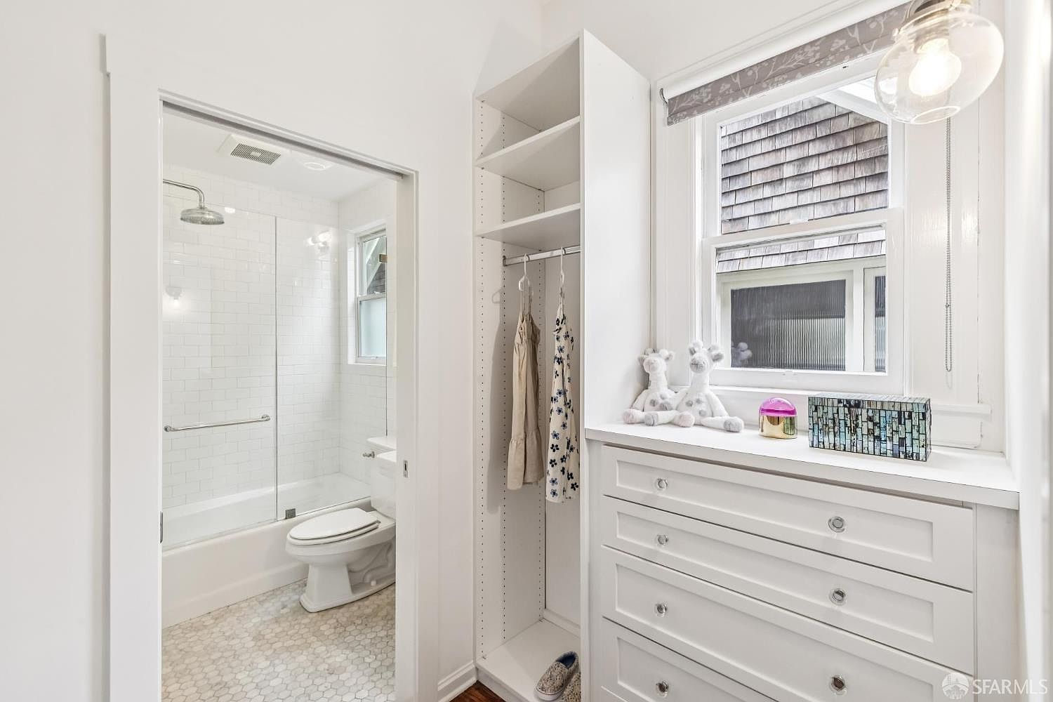This is a bright and clean bathroom featuring a shower-tub combination with white subway tile and a glass enclosure. The floor is tiled with a small hexagonal pattern. Adjacent to the bathroom is a built-in closet and dresser unit, providing ample storage space. The overall impression is fresh and well-organized.