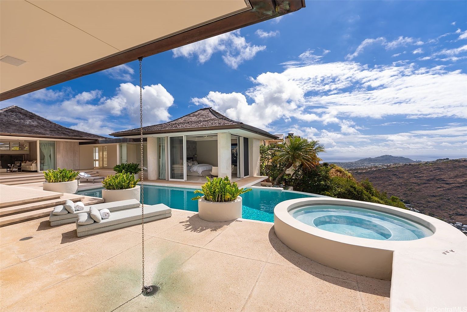 This image showcases a luxurious outdoor pool and spa area of a high-end property. The infinity pool blends seamlessly with the horizon, offering stunning views of the surrounding landscape. A modern jacuzzi sits adjacent to the pool, and lounge chairs are arranged for relaxation, creating an inviting and sophisticated outdoor living space.