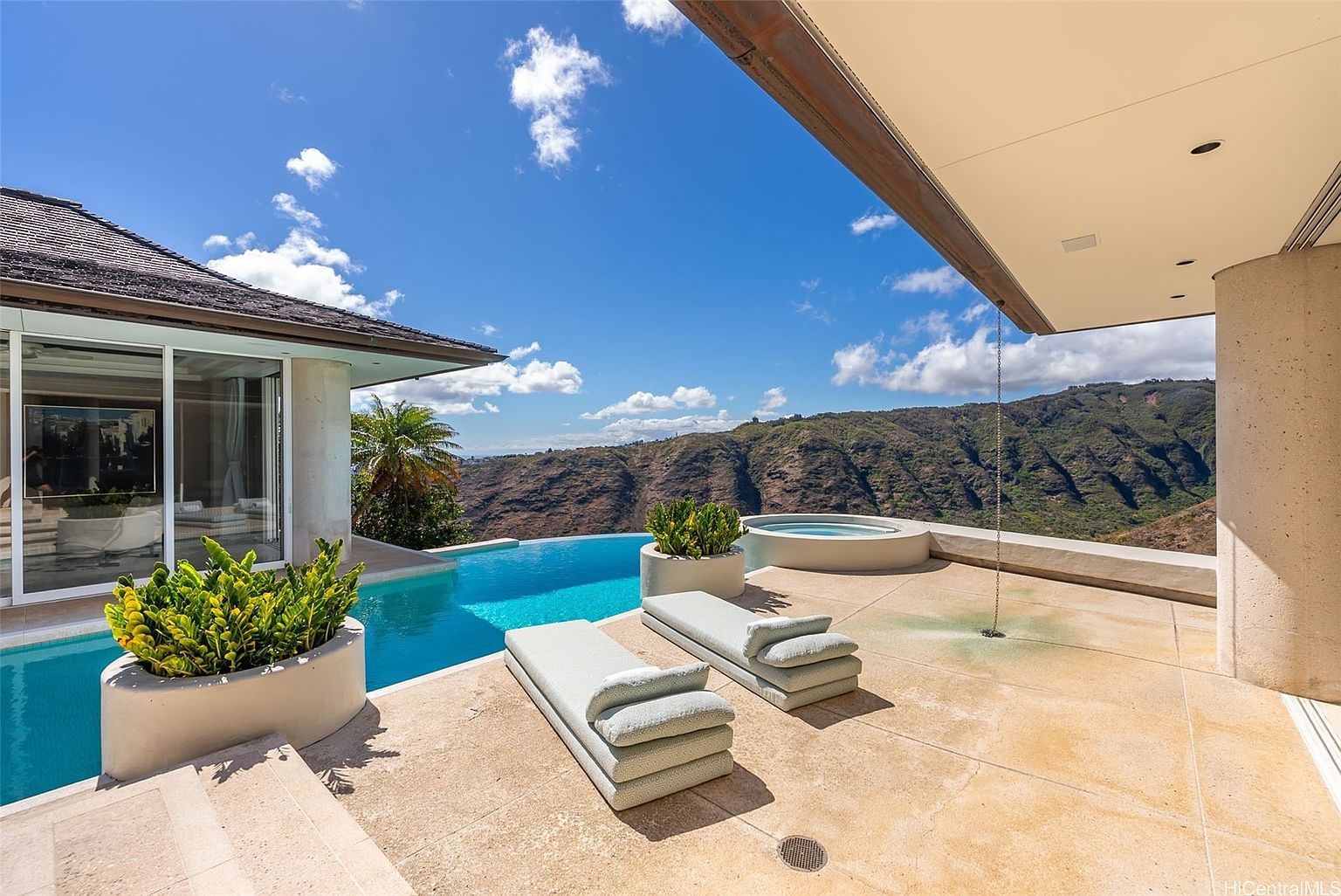 This image showcases a luxurious outdoor pool and spa area with stunning mountain views. Two modern lounge chairs sit on the patio, complemented by potted plants, creating a relaxing atmosphere. The infinity pool blends seamlessly with the landscape, enhancing the property's appeal.