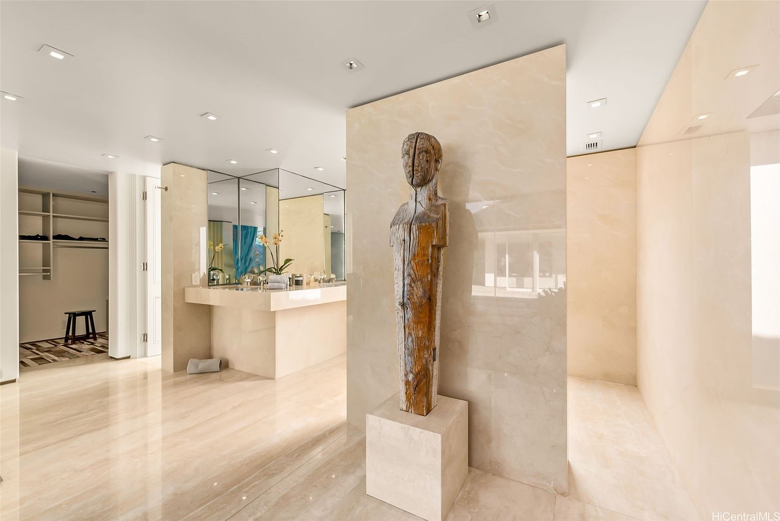 This is a luxurious primary bathroom featuring a modern design with marble flooring and walls. A unique wooden sculpture stands prominently, adding an artistic touch. The bathroom includes a vanity with mirrored walls and a separate shower area, creating a spa-like atmosphere.