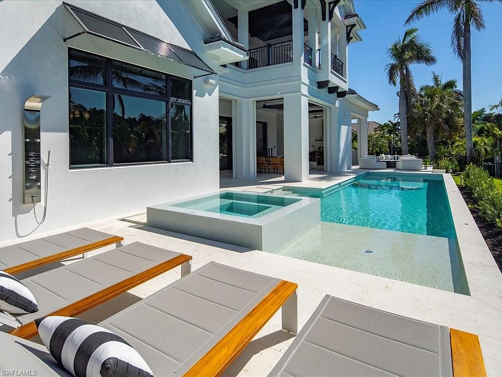 This image showcases a luxurious outdoor pool and spa area of a modern home. The pool features a shallow lounging area and is adjacent to a raised spa with tiled detailing. Several lounge chairs are arranged on the surrounding patio, suggesting a relaxing and upscale outdoor living space.