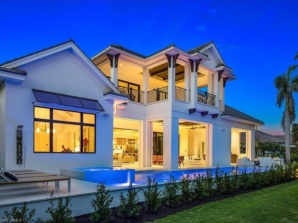 This is a rear view of a luxurious two-story home featuring a modern architectural design. The house boasts a large swimming pool with integrated spa, surrounded by manicured landscaping and a well-maintained lawn. The open-concept design allows for seamless indoor-outdoor living, with large windows and doors providing ample natural light and access to the outdoor space.