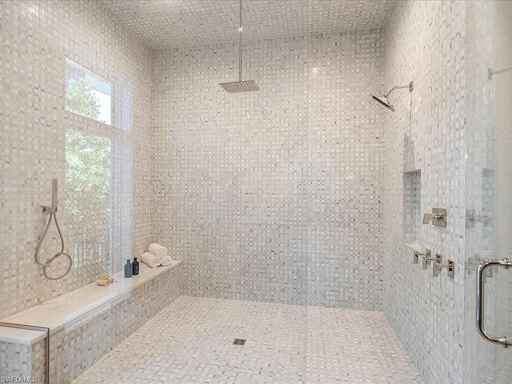 This is a luxurious primary bathroom featuring a spacious walk-in shower with mosaic tile covering the walls, ceiling, and floor. The shower includes both a rainfall showerhead and a handheld shower fixture, along with built-in shelving and a bench. The overall impression is clean, modern, and spa-like.