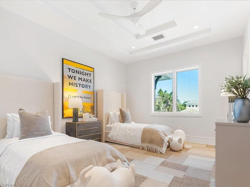 This is a bright and airy guest bedroom featuring two twin beds with neutral-toned bedding and upholstered headboards. A large framed art piece adds a pop of color, while a window provides natural light and a view of the outdoors. The room is decorated in a minimalist style with a focus on comfort and functionality, making it an inviting space for guests.