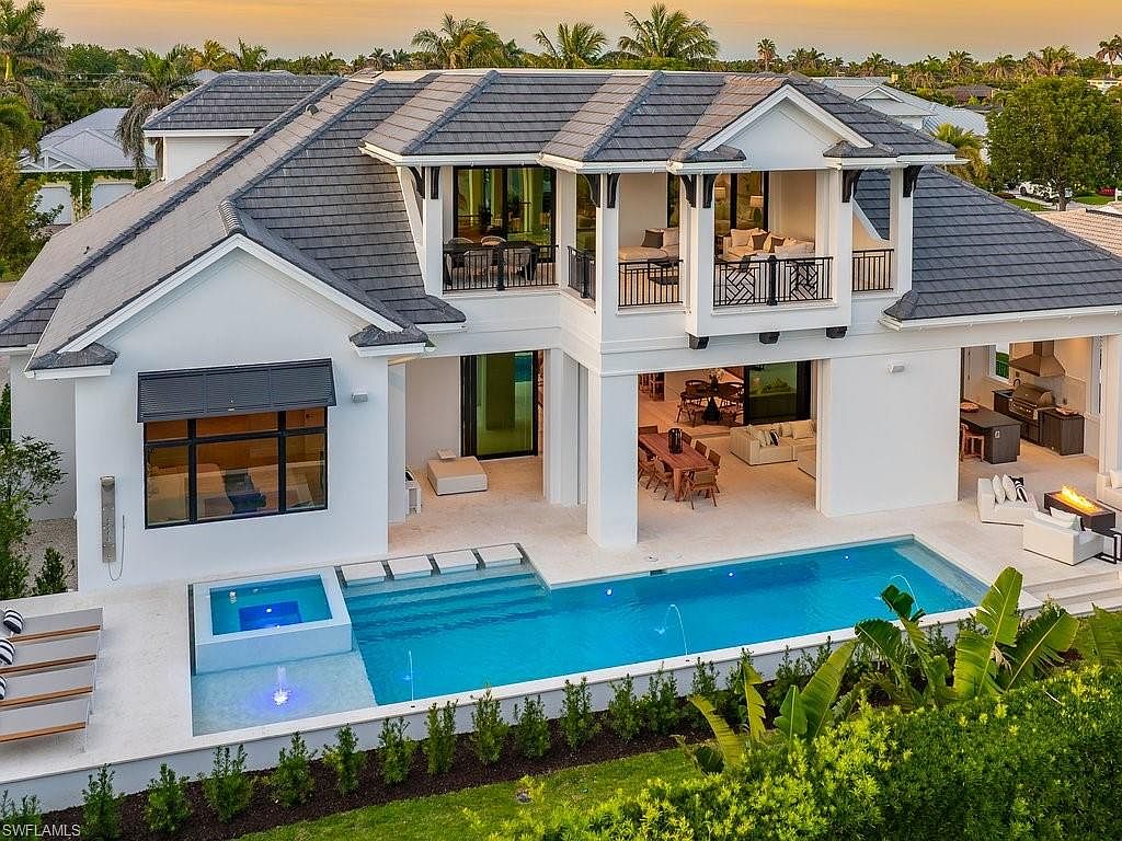 This image showcases the rear exterior of a luxurious home, highlighting a stunning pool and spa area. The pool features a modern design with clean lines and a built-in spa, surrounded by a spacious patio perfect for entertaining. The architecture is contemporary with a white exterior, dark roof, and open-air living spaces, creating an inviting and upscale outdoor oasis.