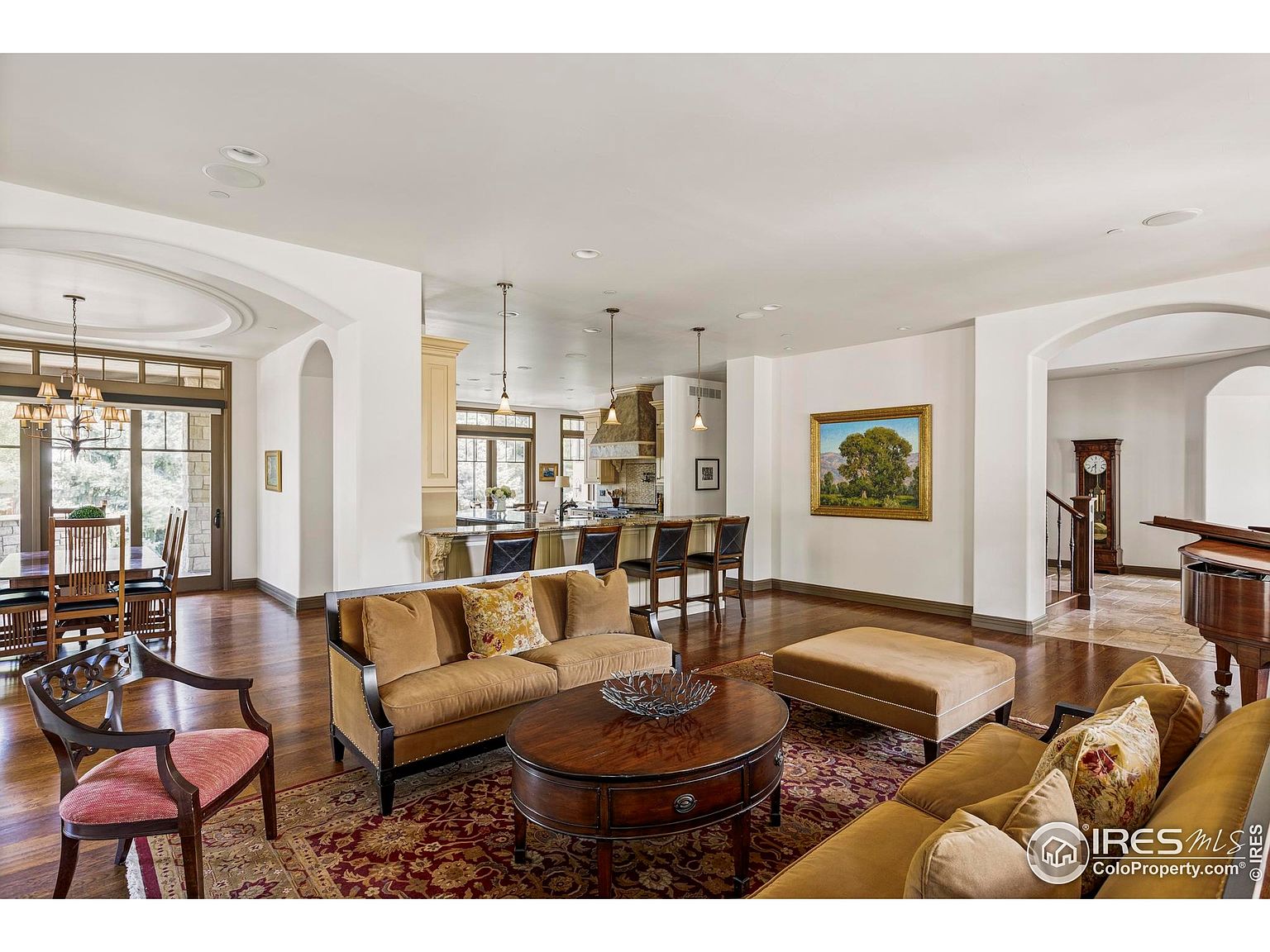 This is an interior shot of a luxurious living room that seamlessly blends into the kitchen and dining area. The living room features two plush sofas, a round wooden coffee table, and an ottoman, all set upon an ornate rug. The open floor plan allows for easy flow between the spaces, enhancing the home's appeal for entertaining and daily living.