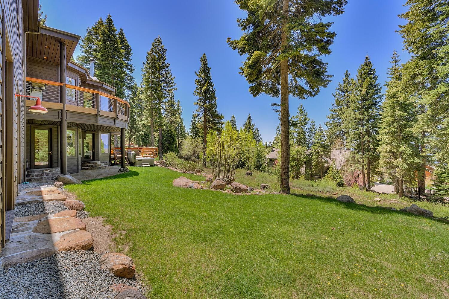 This image showcases a beautifully landscaped backyard with a lush green lawn, mature trees, and natural stone accents. A multi-level deck and patio area extend from the house, offering ample space for outdoor entertaining. The setting exudes a sense of tranquility and privacy, making it an ideal outdoor retreat.