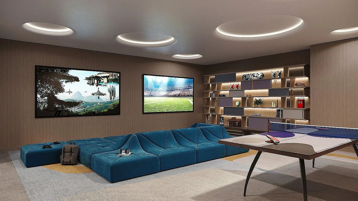 This contemporary recreation room features a large, modular blue sofa set against wood-paneled walls, creating a comfortable lounge area. The space is equipped with two wall-mounted televisions and a ping-pong table, complemented by a large, illuminated shelving unit for storage and display. Recessed circular lighting fixtures in the ceiling provide a modern aesthetic to this versatile entertainment space.