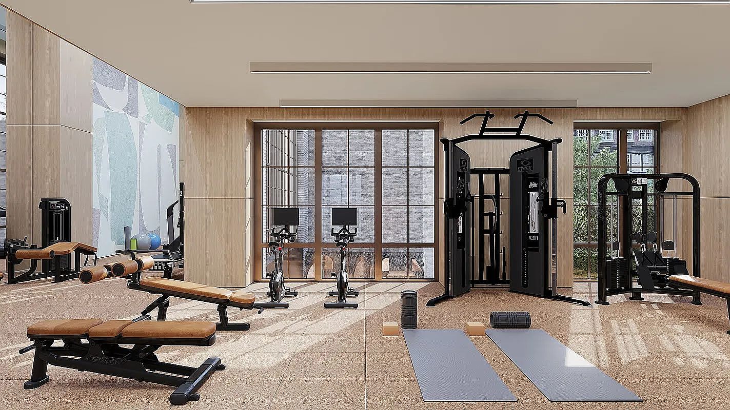 This modern, well-lit home gym features a variety of professional-grade fitness equipment, including a multi-station cable machine, stationary bikes, and adjustable weight benches. The space is finished with light wood-toned wall paneling and a durable, textured floor, creating a clean and inviting atmosphere. Large windows provide ample natural light and views of the exterior, enhancing the open and airy feel of the workout area.