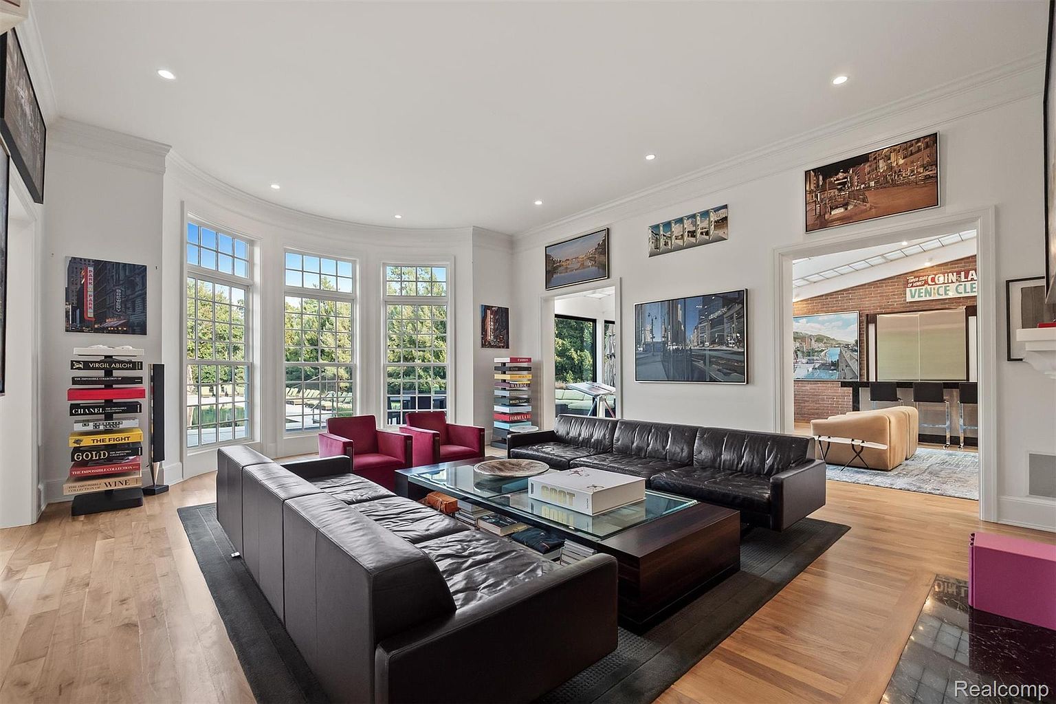 This is a spacious and luxurious living room featuring hardwood floors, large windows, and recessed lighting. The room is furnished with two large leather sofas, two red armchairs, and a glass-topped coffee table. Artwork adorns the walls, and the overall impression is one of elegance and comfort.