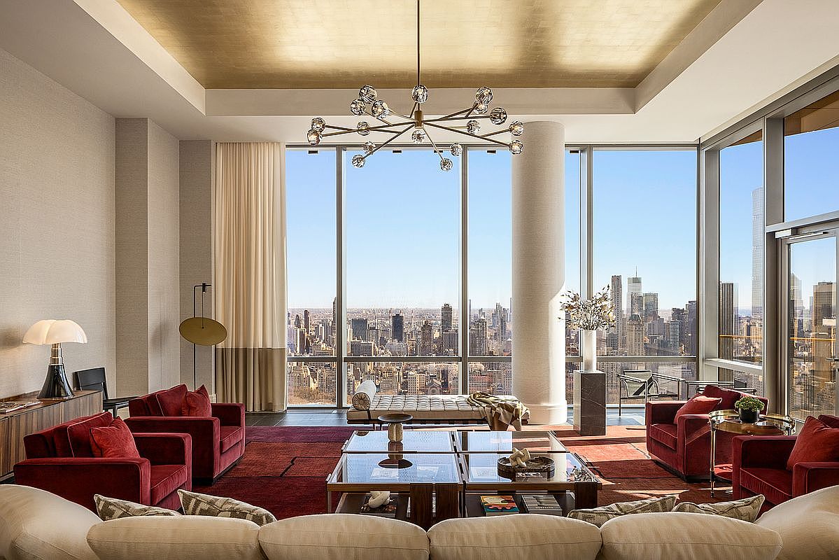 This luxurious, high-rise living room features a sophisticated design with a deep red color palette, plush velvet armchairs, and a large, comfortable sofa. The space is anchored by a striking modern chandelier and a gold-leaf ceiling, while floor-to-ceiling windows provide a breathtaking, panoramic view of the city skyline. The overall impression is one of refined elegance and urban opulence, perfectly suited for high-end metropolitan living.