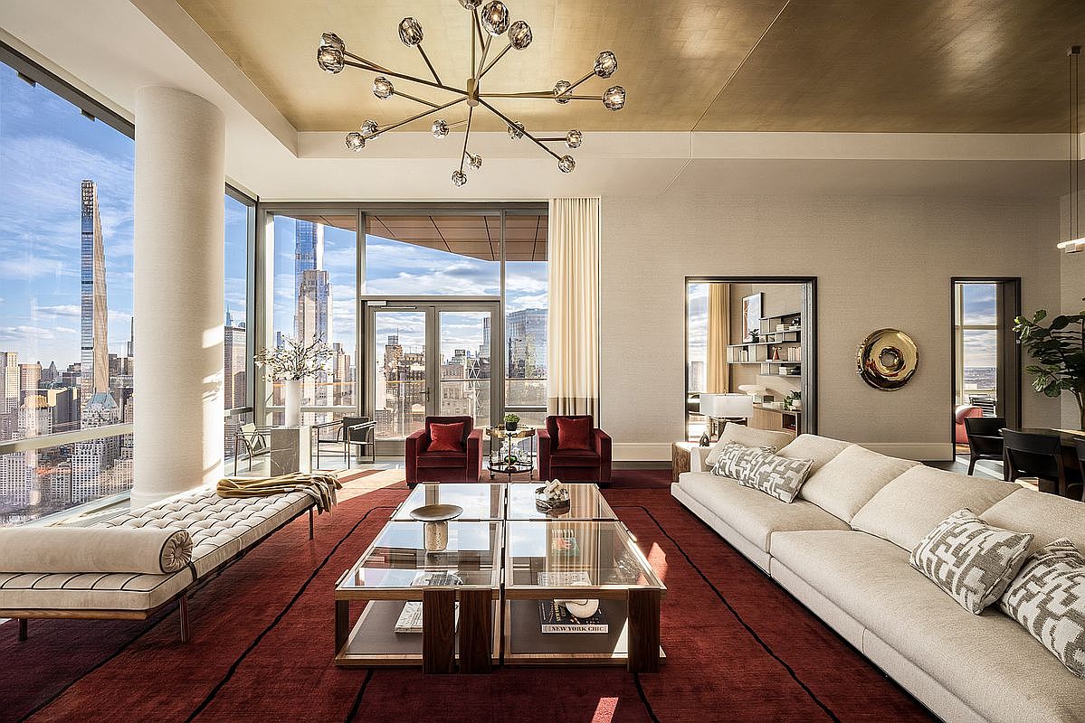 This luxurious, high-rise living room features floor-to-ceiling windows that offer a breathtaking panoramic view of the New York City skyline. The space is anchored by a deep red area rug, a large cream-colored sofa, and a sophisticated glass-topped coffee table, all illuminated by a striking, modern sputnik-style chandelier. The room exudes an air of refined elegance, enhanced by a gold-leaf ceiling and a seamless transition to an outdoor terrace.