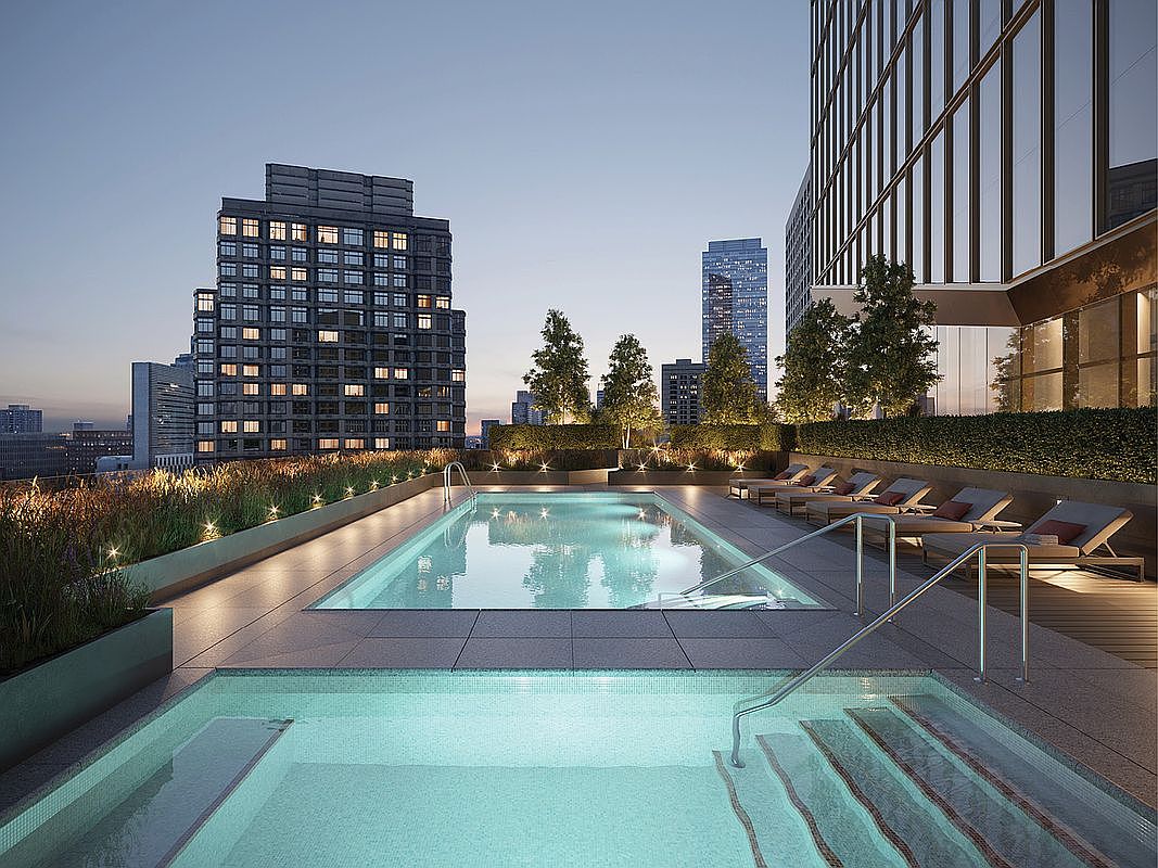 This high-end rooftop terrace features a pristine swimming pool and a separate hot tub, set against a stunning urban skyline at dusk. The area is elegantly landscaped with manicured hedges and modern lounge seating, creating a sophisticated and tranquil atmosphere for residents. The perspective is a low-angle shot from the edge of the hot tub, emphasizing the seamless integration of luxury amenities with the city view.