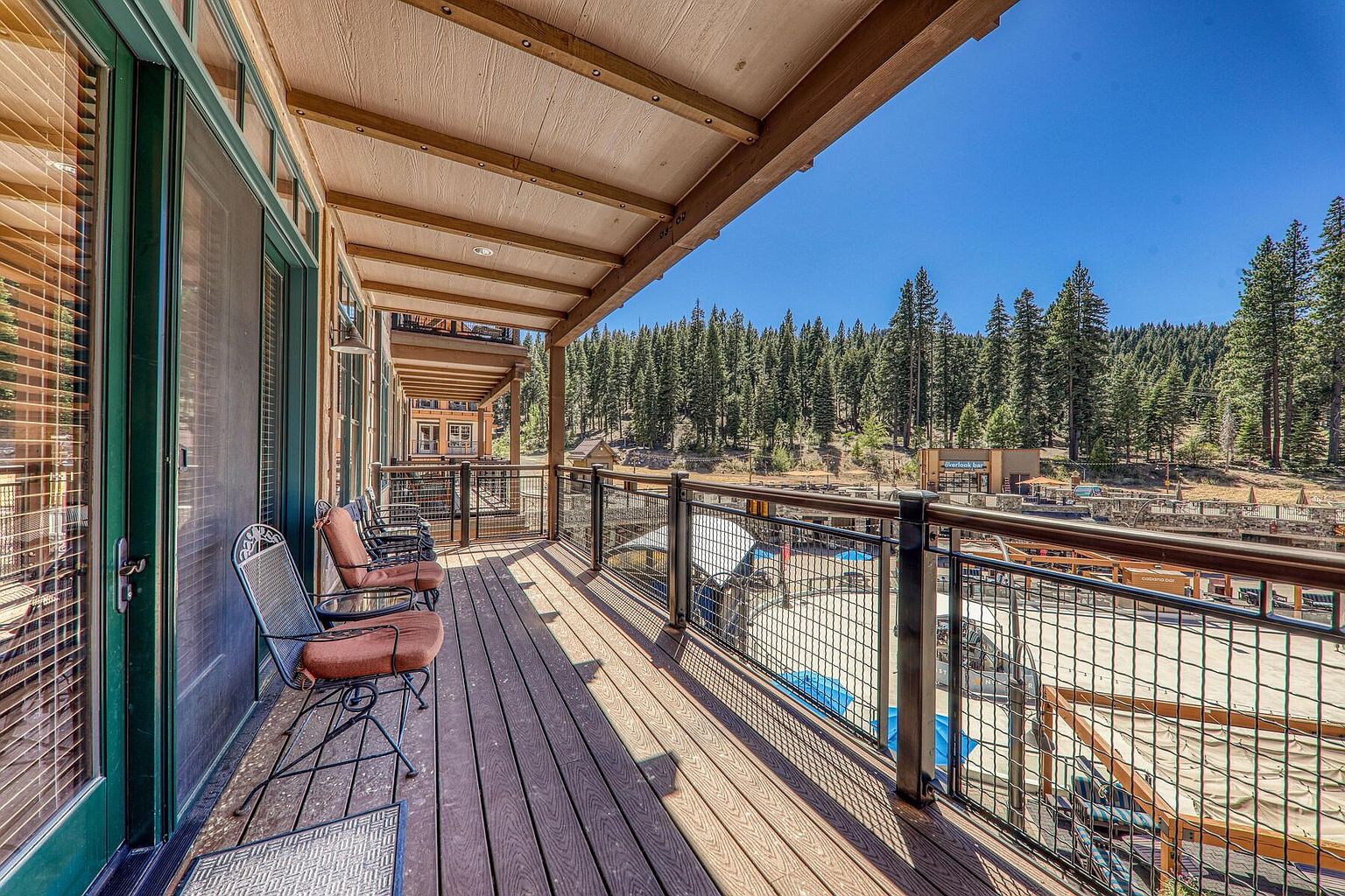This image showcases a spacious balcony with wooden decking and a metal railing, offering a view of a lush forest and a nearby commercial area. The balcony features comfortable seating, suggesting a relaxing outdoor living space. The overall impression is one of tranquility and connection with nature, making it an appealing feature for potential buyers.
