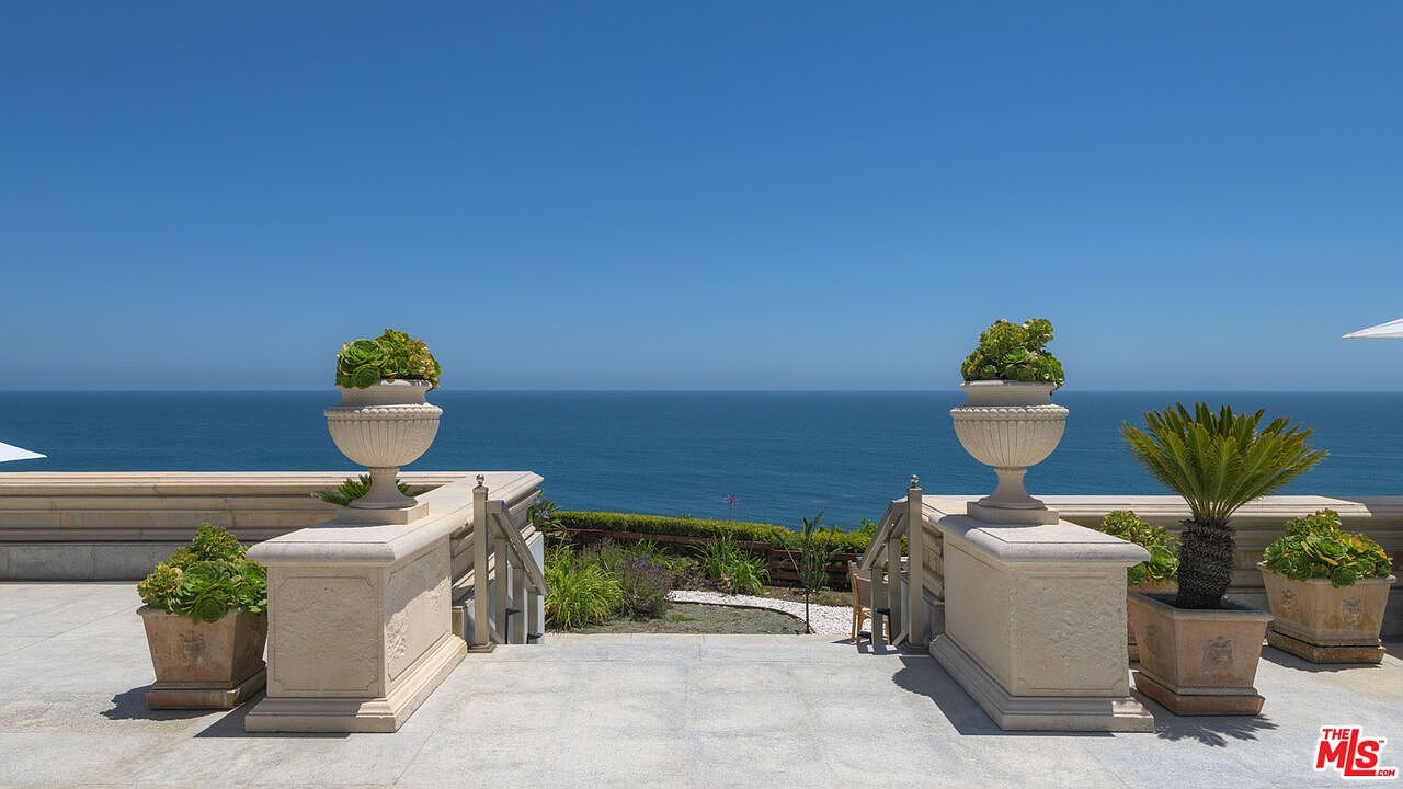 This image showcases a luxurious patio or balcony with stunning ocean views. The space is adorned with elegant planters and decorative urns, adding a touch of sophistication. The design incorporates stone elements and a clear view of the horizon, creating a serene and upscale outdoor living area.