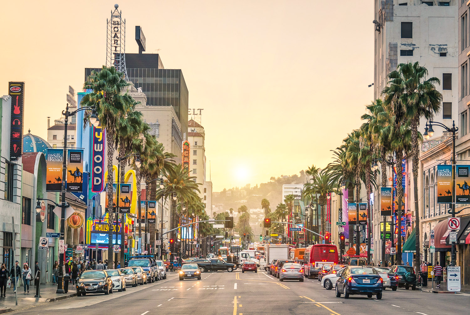 This vibrant street scene showcases the iconic Hollywood Boulevard. Lined with palm trees, historic buildings, banners, and plenty of vehicular traffic. Represents a bustling urban location, reflecting the energy and tourist appeal for surrounding commercial and residential real estate.