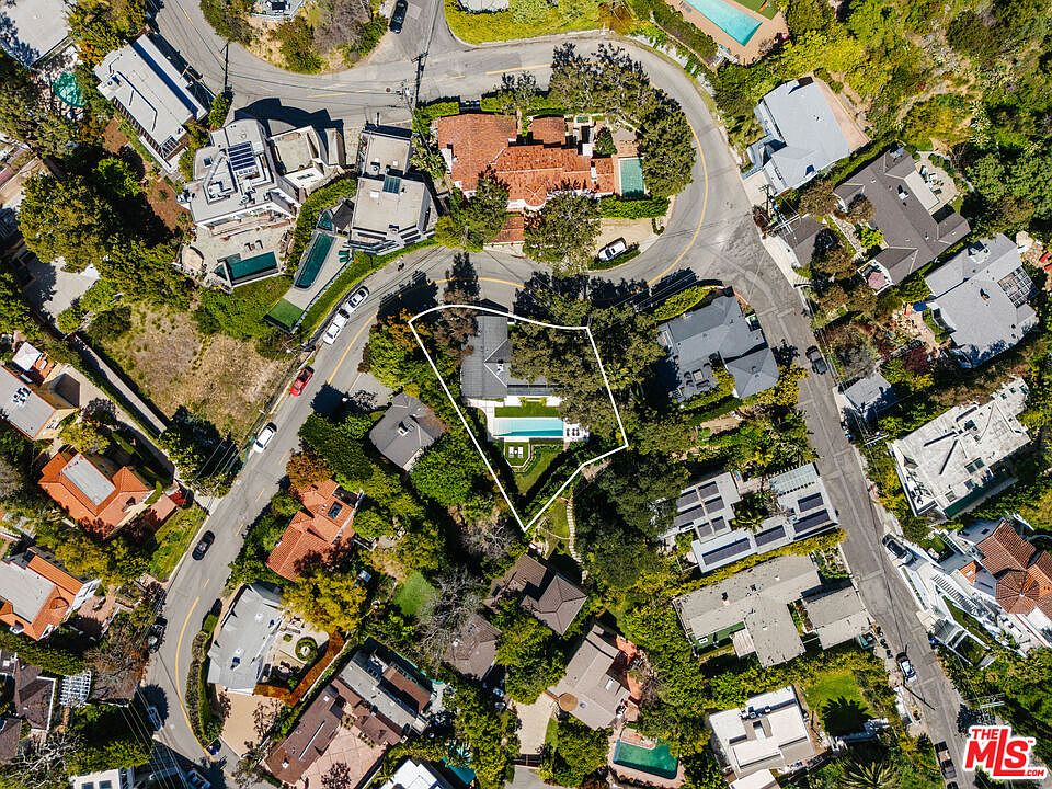 This aerial view showcases a luxurious property nestled among lush greenery and neighboring homes. The house features a well-maintained yard with a sparkling pool, surrounded by mature trees and manicured landscaping. The overall impression is one of privacy and exclusivity in a desirable residential area.
