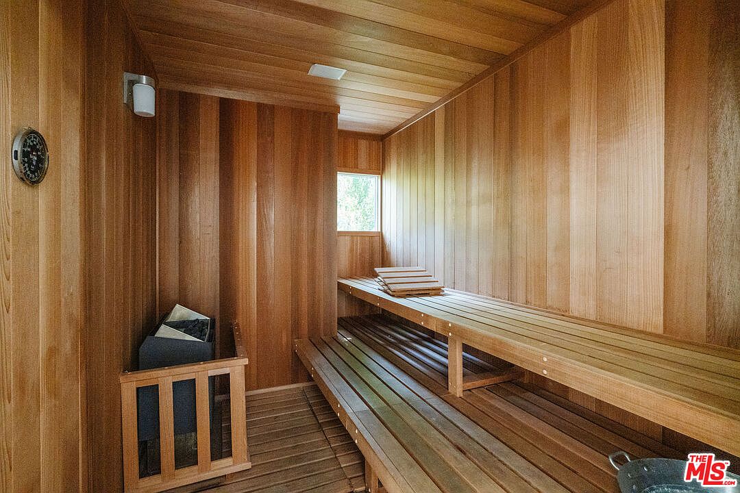 This is an interior shot of a sauna, featuring wooden walls, ceiling, and tiered benches. A small window provides natural light, and a heater is visible in the corner. The overall impression is a clean and relaxing space, perfect for unwinding.