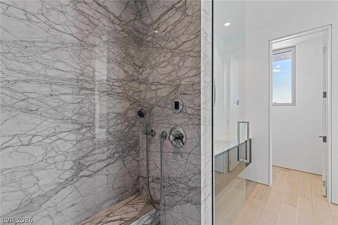 This image captures a modern shower enclosure featuring striking, high-contrast patterned stone walls and a built-in stone bench. A glass partition separates the shower from the adjacent bathroom area, which features light wood flooring and a doorway leading to another space. The perspective highlights the clean lines and contemporary design of the shower fixtures and the seamless transition between the tiled shower and the rest of the room.