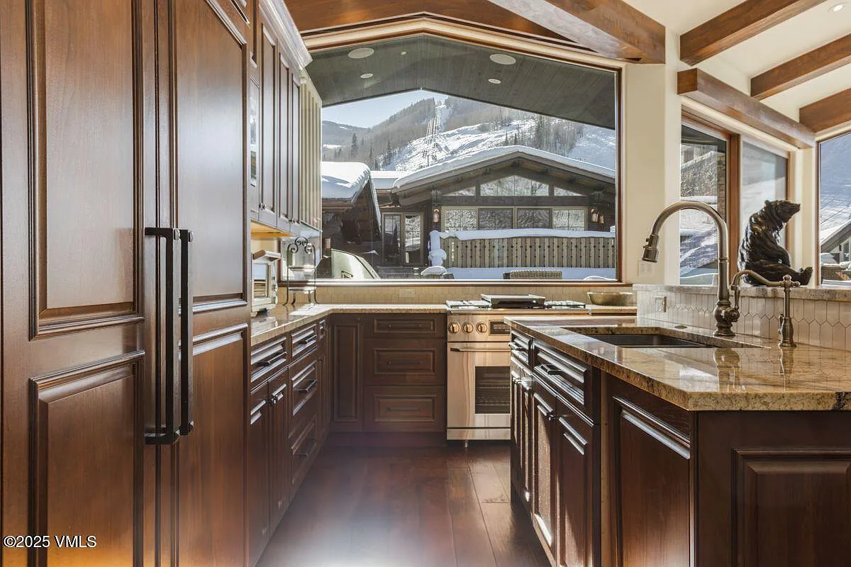 This kitchen features rich wood cabinetry and granite countertops. A large window provides a stunning view of the snow-covered landscape outside. Stainless steel appliances add a modern touch to the classic design.