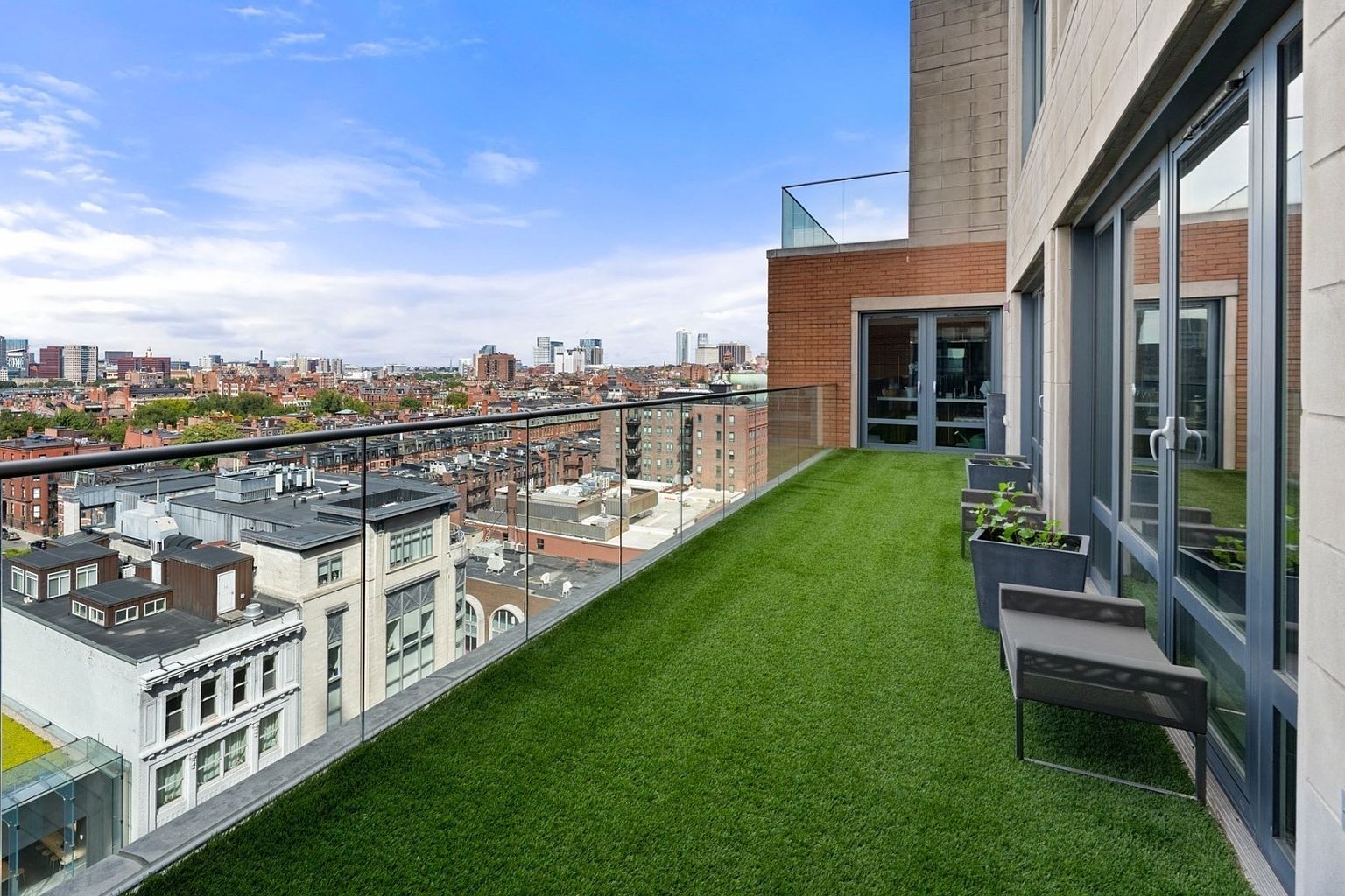 This image showcases a luxurious balcony with artificial turf, offering a stunning cityscape view. The balcony features modern glass railings, potted plants, and stylish outdoor seating, creating an inviting and sophisticated outdoor living space. The building's architectural details and the expansive view enhance the property's appeal.