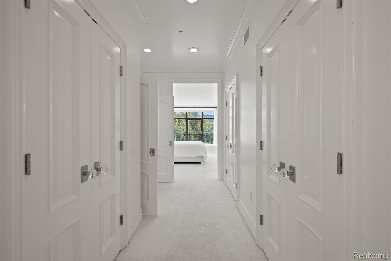 The image showcases a bright, elegant hallway with white walls, doors, and carpet. The hallway features multiple doors with crystal knobs, leading to different rooms, and a view into a bedroom with a large window at the end. The overall impression is clean, modern, and luxurious.