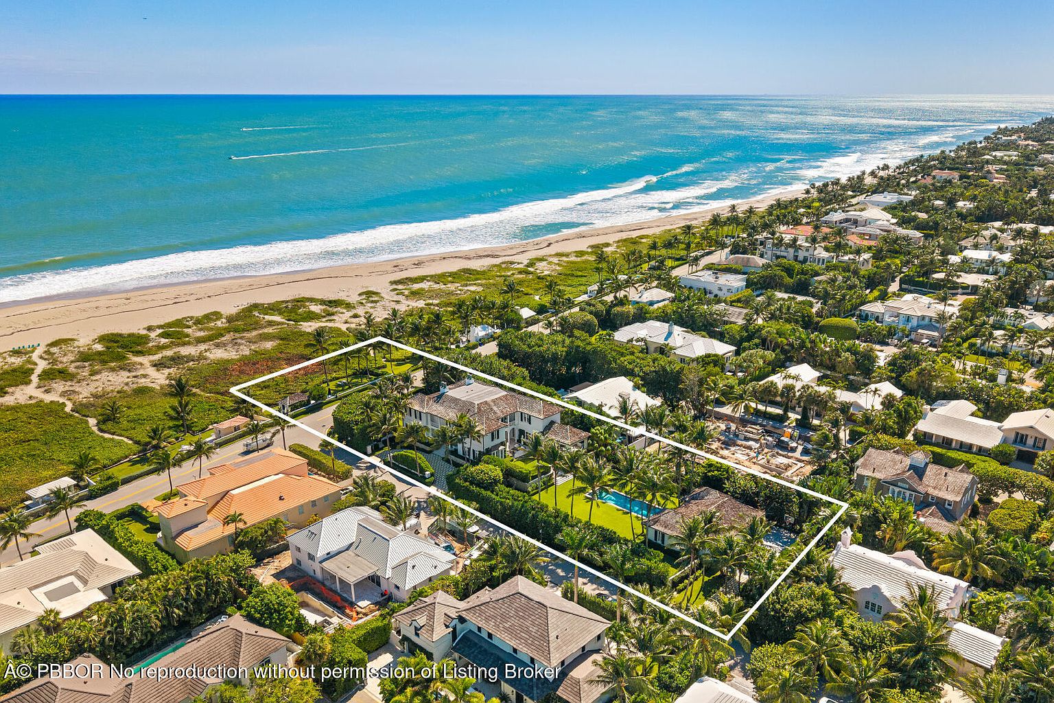 This aerial view showcases a luxurious beachfront property with lush landscaping, a swimming pool, and direct access to the ocean. The house is surrounded by mature trees and manicured lawns, providing privacy and a serene atmosphere. The overall impression is one of exclusivity and coastal elegance.
