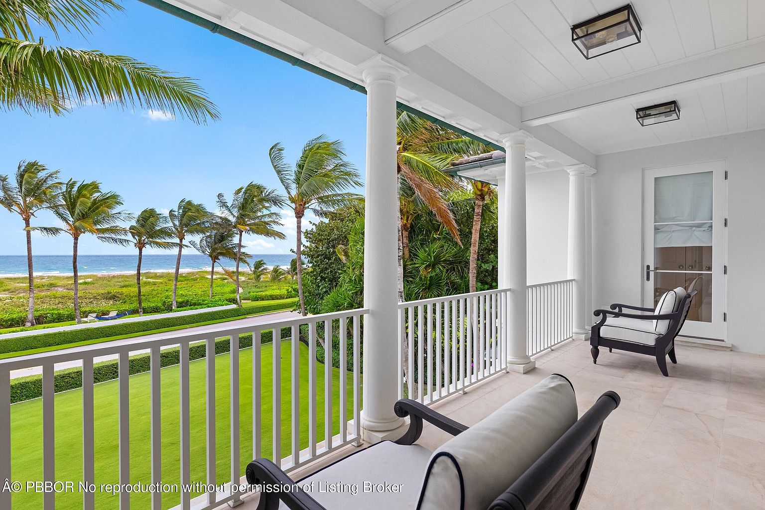 This image showcases a luxurious balcony with a stunning ocean view framed by palm trees. The balcony features white columns and railings, creating a classic and elegant aesthetic. Comfortable seating arrangements invite relaxation, while the tiled flooring adds a touch of sophistication to this outdoor living space.