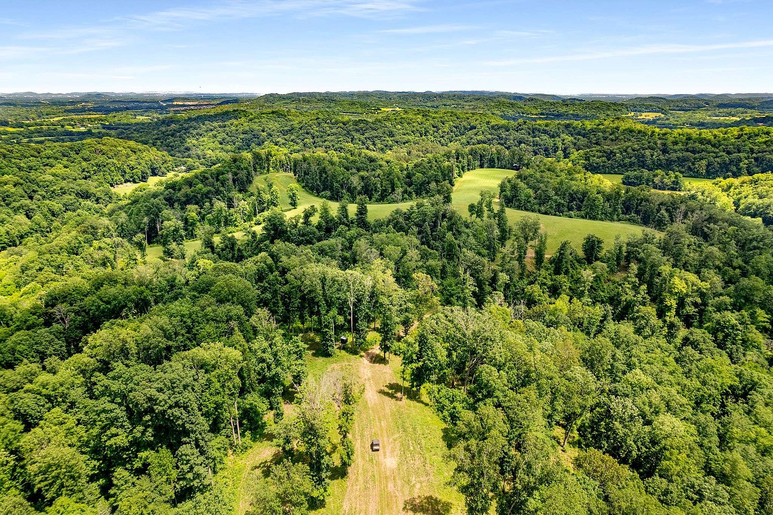 This aerial view showcases a vast expanse of lush, green forested land with interspersed clearings and rolling hills. The landscape is dominated by dense trees, creating a sense of natural beauty and seclusion. The perspective offers a comprehensive view of the property's size and potential, ideal for highlighting its expansive acreage.
