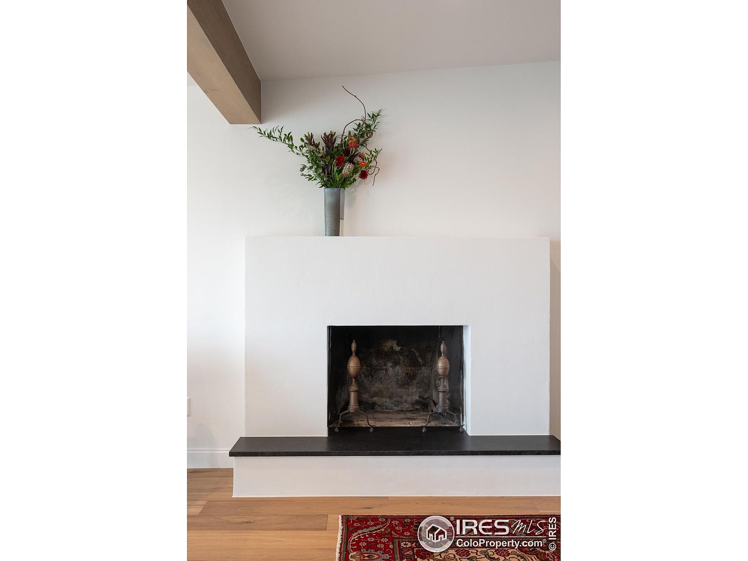 The image showcases a modern living room featuring a minimalist fireplace with a white surround and a dark hearth. A vase of flowers sits atop the mantel, adding a touch of color to the neutral palette. The room exudes a clean and sophisticated aesthetic, emphasizing simplicity and elegance.