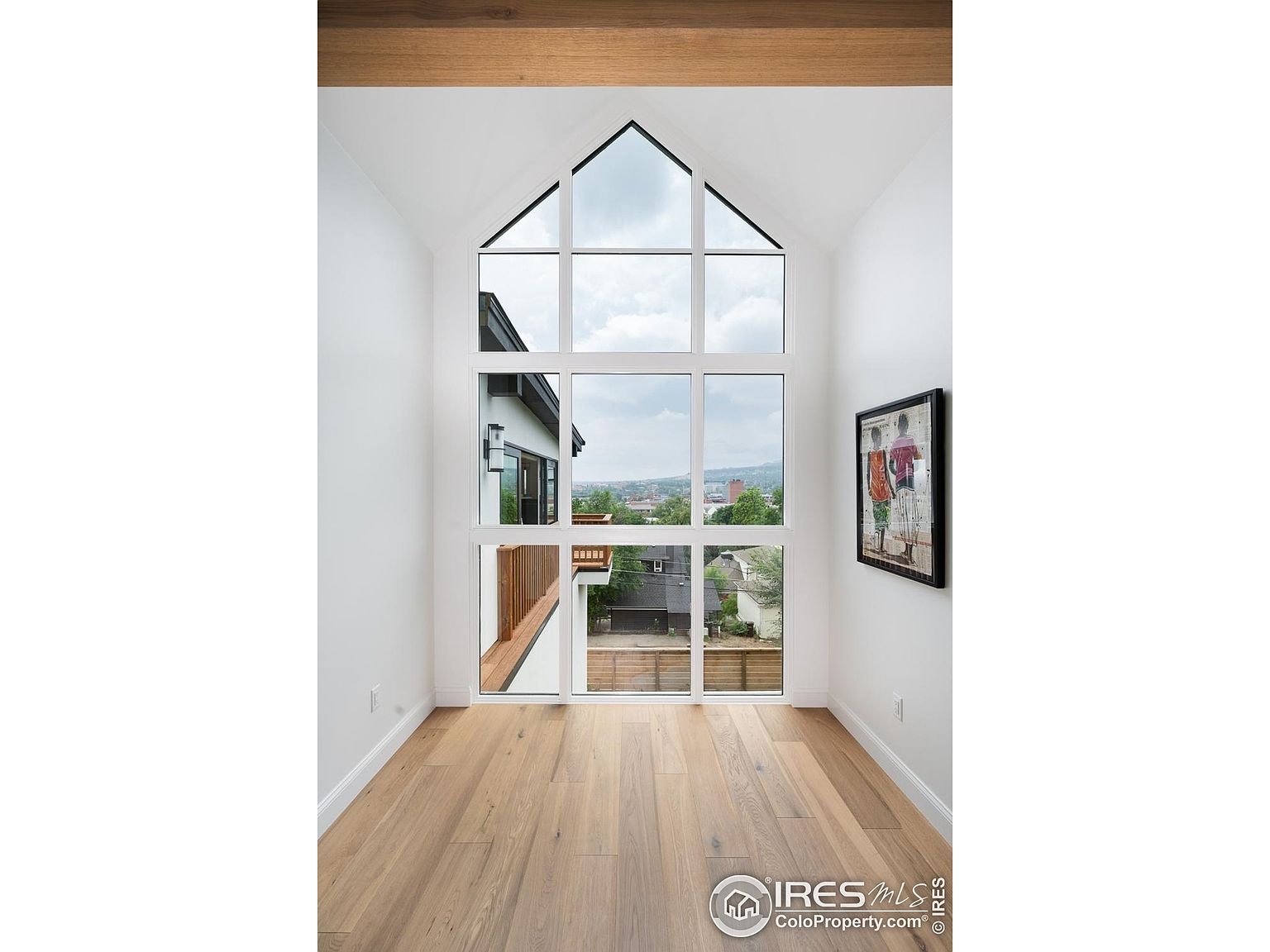 This interior shot showcases a bright hallway with a striking, multi-paned window that offers an exterior view. The light wood flooring adds warmth to the space, while the white walls and trim create a clean, modern aesthetic. A framed piece of art hangs on the right wall, adding a touch of personality.