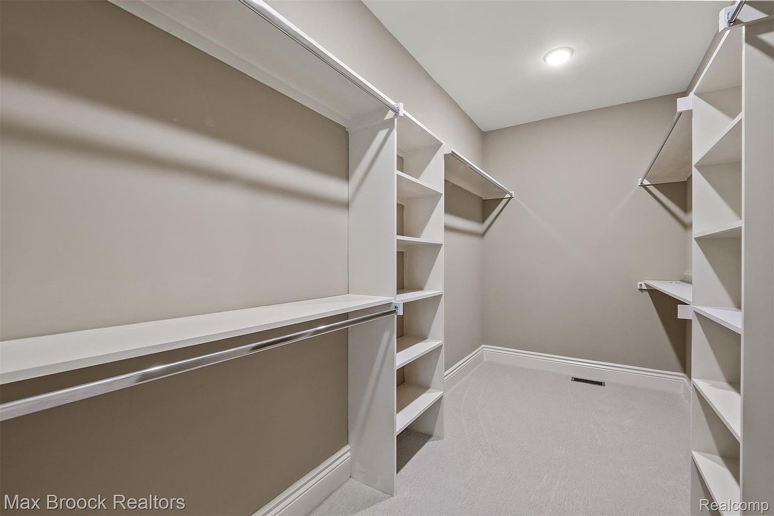 This is a well-organized walk-in closet featuring custom shelving and hanging rods. The closet is painted in neutral tones, with white shelving units and light gray walls. The space is well-lit, creating a clean and inviting atmosphere, perfect for showcasing storage capabilities.
