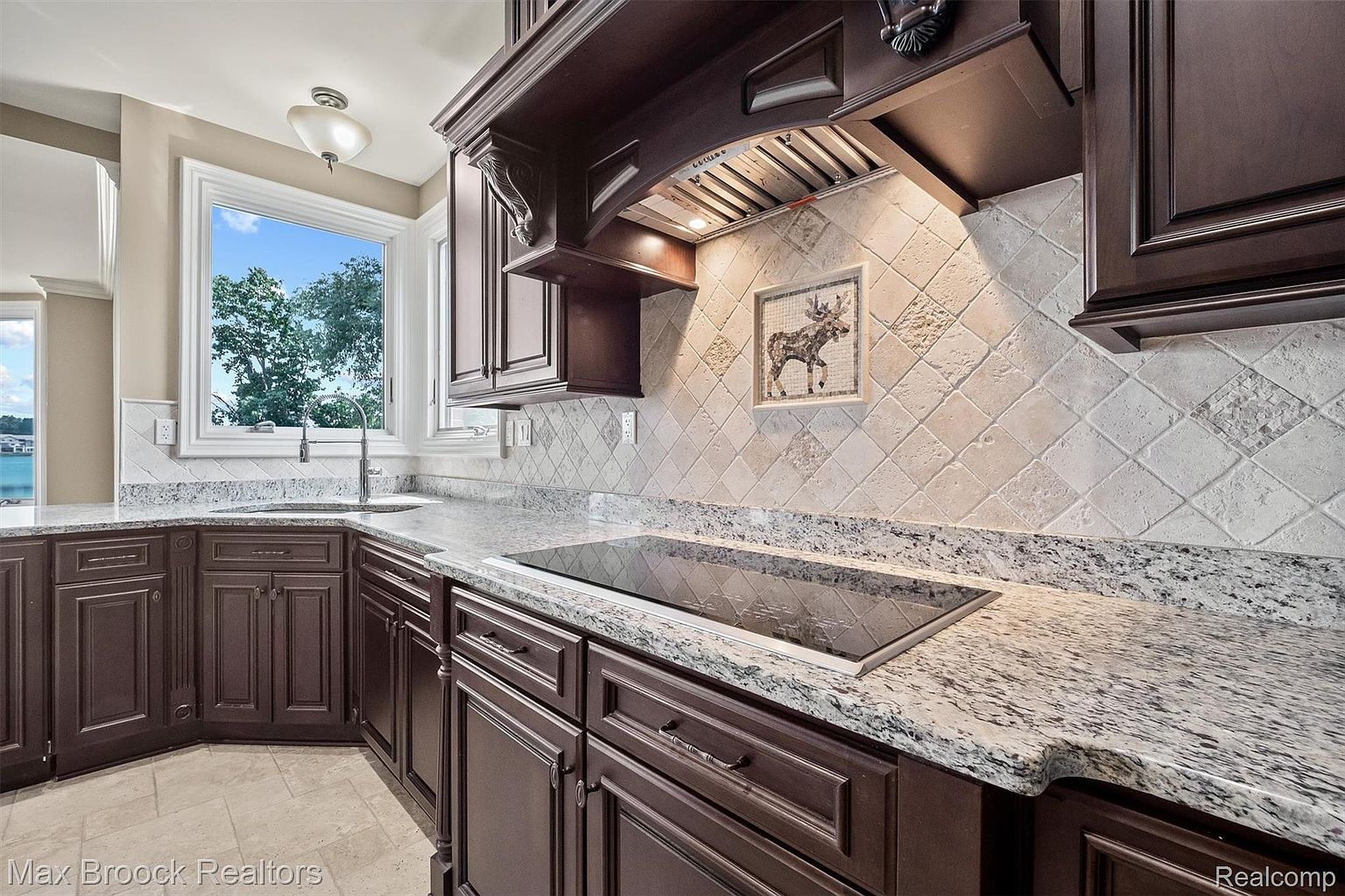 This is a well-appointed kitchen featuring dark wood cabinetry, granite countertops, and a decorative tile backsplash. A modern cooktop is integrated into the countertop, and a window provides natural light. The overall impression is one of warmth and sophistication.