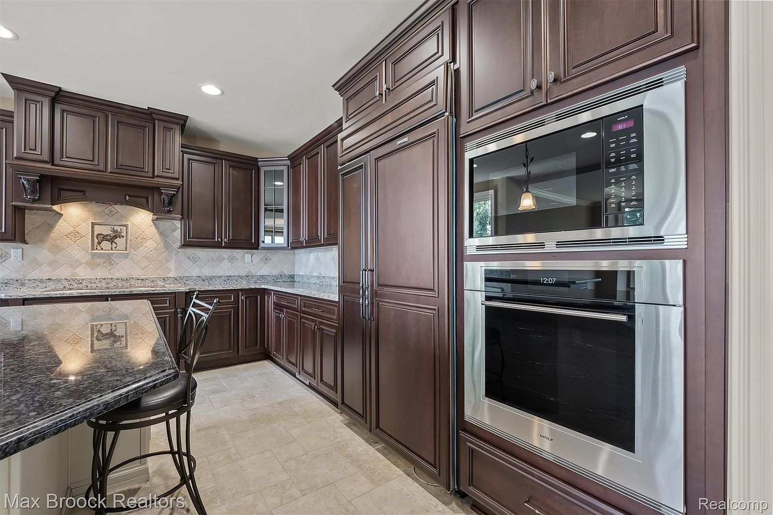 This is a well-appointed kitchen featuring dark wood cabinetry, stainless steel appliances, and granite countertops. The kitchen includes a built-in refrigerator and a double oven, suggesting a high-end finish. The overall impression is one of luxury and functionality.